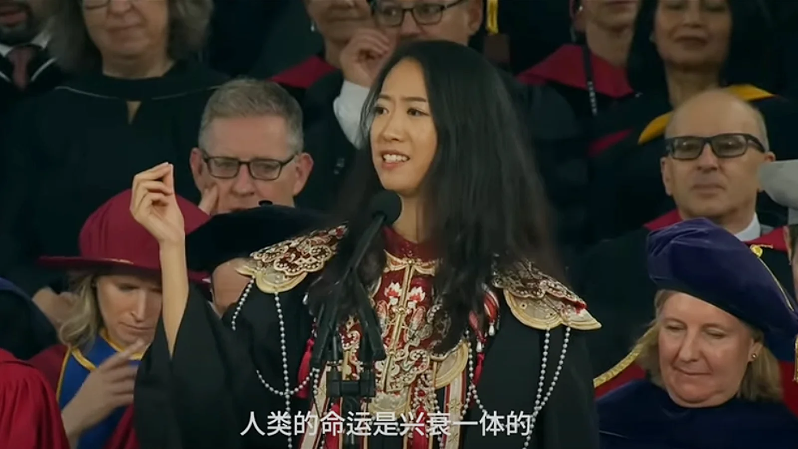 中国女生蔣雨融在哈佛毕业典礼上发表演讲，身穿刺绣服饰，站在讲台前发言。