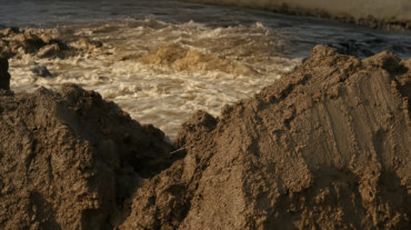 水库清淤作业中，泥浆被挖起堆放在岸边，象征“泥浆变成金”的资源再生。